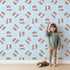 Lovely child standing in front of Whimsy Tots Moo Moo Love Wallpaper in Blue with cow, heart, bell in design.