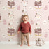 Lovely child standing in front of Whimsy Tots Moo Farm Friends Wallpaper in Pink with cow, bottle, bell, wheat, sign in design.