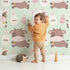 Lovely child standing in front of Whimsy Tots Moo Moo Milk Parade Wallpaper in Green with cow, bottle, bell, dot in design.