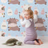 Lovely child standing in front of Whimsy Tots Moo Moo Milk Parade Wallpaper in Blue with cow, bottle, bell, dot in design.