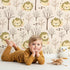 Lovely child standing in front of Whimsy Tots Little Lion Nap Wallpaper in Cream with lion, tree, footprint in design.