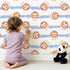 Lovely child standing in front of Whimsy Tots Striped Safari Cubs Wallpaper in Blue with lion, stripe, paw in design.
