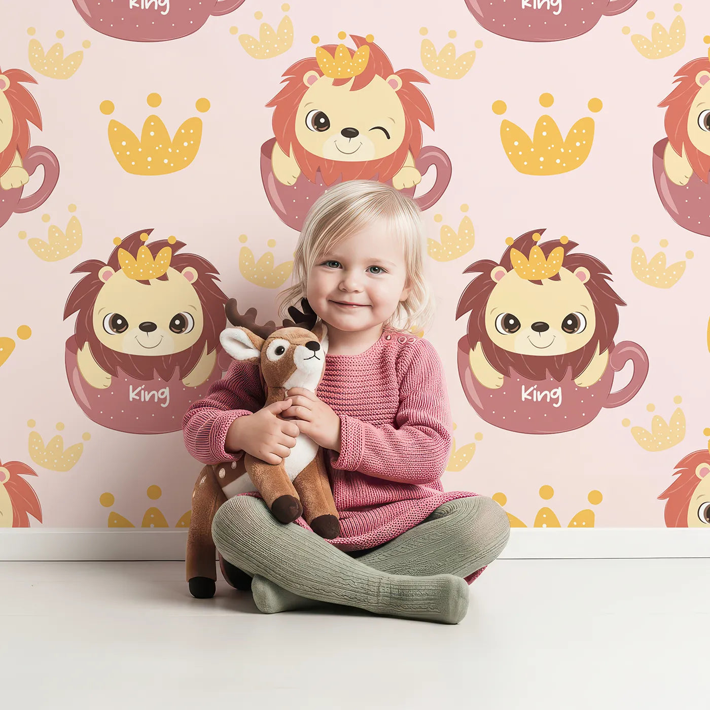 Lovely child standing in front of Whimsy Tots Little King of the Jungle Wallpaper in Pink with lion, crown, teacup in design.