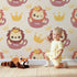 Lovely child standing in front of Whimsy Tots Little King of the Jungle Wallpaper in Beige with lion, crown, teacup in design.