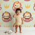 Lovely child standing in front of Whimsy Tots Little King of the Jungle Wallpaper in Mint Green with lion, crown, teacup in design.