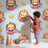Lovely child standing in front of Whimsy Tots Little King of the Jungle Wallpaper in Blue with lion, crown, teacup in design.