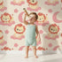 Lovely child standing in front of Whimsy Tots Starry Safari Dreams Wallpaper in Beige with lion, cloud, moon, star in design.