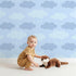 Lovely child standing in front of Whimsy Tots Dreamy Drizzle Clouds Wallpaper in Blue with cloud, star, sprinkle in design.