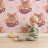 Lovely child standing in front of Whimsy Tots Lovely Tea Mice Wallpaper in Pink with mouse, cup, sprinkle in design.