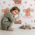 Lovely child standing in front of Whimsy Tots Starry Cloud Mouse Wallpaper in White with mouse, cloud, balloon, star in design.