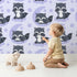 Lovely child standing in front of Whimsy Tots Moonbeam Raccoon Dreams Wallpaper in Purple with raccoon, moon, cloud, star in design.