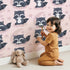 Lovely child standing in front of Whimsy Tots Moonbeam Raccoon Dreams Wallpaper in Pink with raccoon, moon, cloud, star in design.