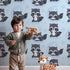 Lovely child standing in front of Whimsy Tots Moonbeam Raccoon Dreams Wallpaper in Blue with raccoon, moon, cloud, star in design.