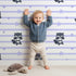 Lovely child standing in front of Whimsy Tots Starlit Raccoon Stripes Wallpaper in Lavender with raccoon, star, stripe in design.