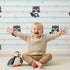 Lovely child standing in front of Whimsy Tots Starlit Raccoon Stripes Wallpaper in Blue with raccoon, star, stripe in design.