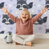 Lovely child standing in front of Whimsy Tots Raccoon Dream Stars Wallpaper in Purple with raccoon, star in design.