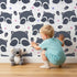 Lovely child standing in front of Whimsy Tots Winkie Raccoon Pals Wallpaper with raccoon, dot, paw in design.