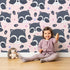 Lovely child standing in front of Whimsy Tots Winkie Raccoon Pals Wallpaper in Pink with raccoon, dot, paw in design.