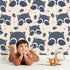 Lovely child standing in front of Whimsy Tots Winkie Raccoon Pals Wallpaper in Cream with raccoon, dot, paw in design.