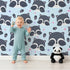Lovely child standing in front of Whimsy Tots Winkie Raccoon Pals Wallpaper in Blue with raccoon, dot, paw in design.