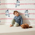Lovely child standing in front of Whimsy Tots Winkie the Zebra Wallpaper in Pink with zebra, stripe in design.