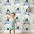 Lovely child standing in front of Whimsy Tots Zebra Snuggle Smiles Wallpaper in Green with zebra, heart, face in design.