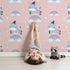 Lovely child standing in front of Whimsy Tots Rainbow Dreamy Zebra Wallpaper in Pink with zebra, rainbow, cloud, star in design.