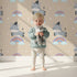 Lovely child standing in front of Whimsy Tots Rainbow Dreamy Zebra Wallpaper in Beige with zebra, rainbow, cloud, star in design.