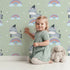 Lovely child standing in front of Whimsy Tots Rainbow Dreamy Zebra Wallpaper in Green with zebra, rainbow, cloud, star in design.