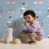Lovely child standing in front of Whimsy Tots Rainbow Dreamy Zebra Wallpaper in Blue with zebra, rainbow, cloud, star in design.