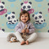Lovely child standing in front of Whimsy Tots Cuddle Cup Panda Wallpaper in Sage Green with panda, cup, star, crown in design.