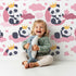Lovely child standing in front of Whimsy Tots Panda Dreamclouds Wallpaper in Pink with panda, cloud, crown, moon, star in design.