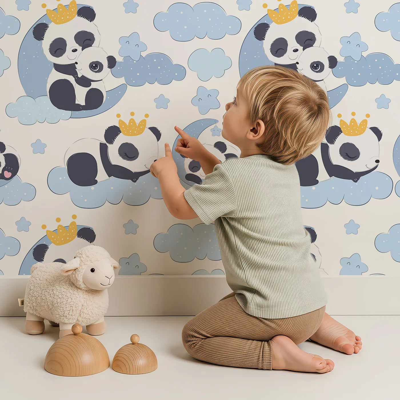 Lovely child standing in front of Whimsy Tots Panda Dreamclouds Wallpaper in Blue with panda, cloud, crown, moon, star in design.