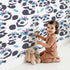 Lovely child standing in front of Whimsy Tots Tribal Hug Panda Wallpaper in White with panda, feather, headband, hug, leaf in design.