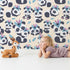 Lovely child standing in front of Whimsy Tots Tribal Hug Panda Wallpaper in Beige with panda, feather, headband, hug, leaf in design.