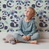 Lovely child standing in front of Whimsy Tots Tribal Hug Panda Wallpaper in Mint Green with panda, feather, headband, hug, leaf in design.