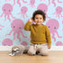 Lovely child standing in front of Whimsy Tots Ocean Bubbles Octopus Wallpaper in Blue with octopus, tentacle, dot, sea in design.