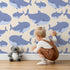 Lovely child standing in front of Whimsy Tots Whale Shark Wiggles Wallpaper in Beige with shark, whale shark, spot, sea in design.