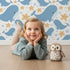 Lovely child standing in front of Whimsy Tots Starry Whale Friends Wallpaper in White with whale, starfish, bubble, dot in design.