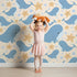 Lovely child standing in front of Whimsy Tots Starry Whale Friends Wallpaper in Cream with whale, starfish, bubble, dot in design.