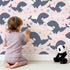 Lovely child standing in front of Whimsy Tots Orca Whale Wonder Wallpaper in Blush Pink with whale, orca, bubble, wave in design.