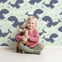 Lovely child standing in front of Whimsy Tots Orca Whale Wonder Wallpaper in Mint Green with whale, orca, bubble, wave in design.