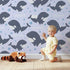 Lovely child standing in front of Whimsy Tots Orca Whale Wonder Wallpaper in Lilac Lavender with whale, orca, bubble, wave in design.