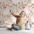 Lovely child standing in front of Whimsy Tots Meadow Hops Bunny Wallpaper in Sand with rabbit, butterfly, flower, leaf in design.