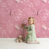 Lovely child standing in front of Whimsy Tots Flutter Garden Butterfly Wallpaper in Rose Pink with butterfly, flower, vine, leaf in design.