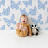Lovely child standing in front of Whimsy Tots Celestial Wings Butterfly Wallpaper in Baby Blue with butterfly, moon, star, swirl in design.