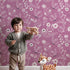 Lovely child standing in front of Whimsy Tots Floral Flutter Butterfly Wallpaper in Berry Pink with butterfly, flower, leaf in design.