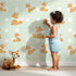 Lovely child standing in front of Whimsy Tots Polka Pals Fox Wallpaper in Mint Green with fox, polka dot, tail, animal in design.