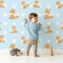Lovely child standing in front of Whimsy Tots Polka Pals Fox Wallpaper in Baby Blue with fox, polka dot, tail, animal in design.