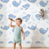 Lovely child standing in front of Whimsy Tots Tweetheart Meadow Wallpaper in Blue with bird, leaf, flower, berry in design.